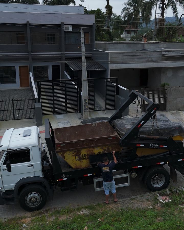 Caminhão branco da Cubas Caçambas levando duas caçambas, parado em frente a casas